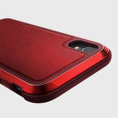 Close-up of the Raptic iPhone XR Case - LUX, showcasing its red textured finish with camera cutout and stylized edges on a gray background. The impact-resistant polycarbonate design combines durability and style.