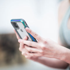 A person holds an iPhone 11 Pro Max encased in the SHIELD by Raptic, a colorful case designed for drop protection, viewed from the side.