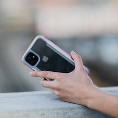 A hand holds an iPhone 11 Pro Max with a dual-camera setup in a Raptic SHIELD clear, sturdy protective case, highlighting drop protection features as it sits on a concrete surface.