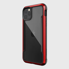 The iPhone 11 Pro Max is equipped with Raptic's SHIELD case, featuring a sleek red and black design. Crafted from aluminum alloy, it offers enhanced drop protection while prominently showcasing its dual camera lenses.