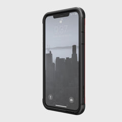 A sleek black iPhone 11 encased in the Raptic SHIELD rests on a light gray background, displaying a cityscape wallpaper. The time is 9:37 on Tuesday, September 26. Designed for protection and wireless charging compatibility, it offers seamless convenience.