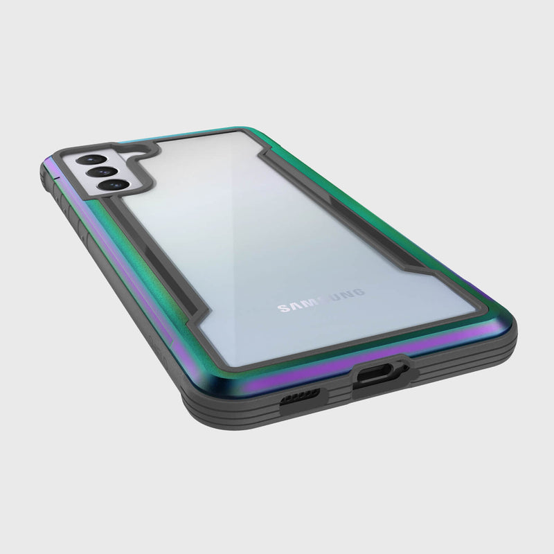 An X-Doria Samsung Galaxy S21 Raptic Shield Iridescent case highlights dual rear cameras, offers military-grade protection, a green and purple iridescent border with a black bottom edge, and remains wireless charging compatible.