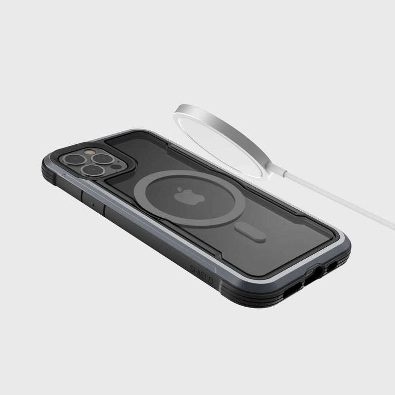 A Raptic SHIELD PRO MAGNET case encases an iPhone 12 on a plain background, while a MagSafe charger hovers above, providing seamless power and reliable drop protection.