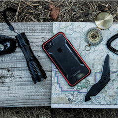 A map, a knife, a flashlight, and an iPhone SE/8/7 Case - SHIELD by Raptic are on a wooden table.