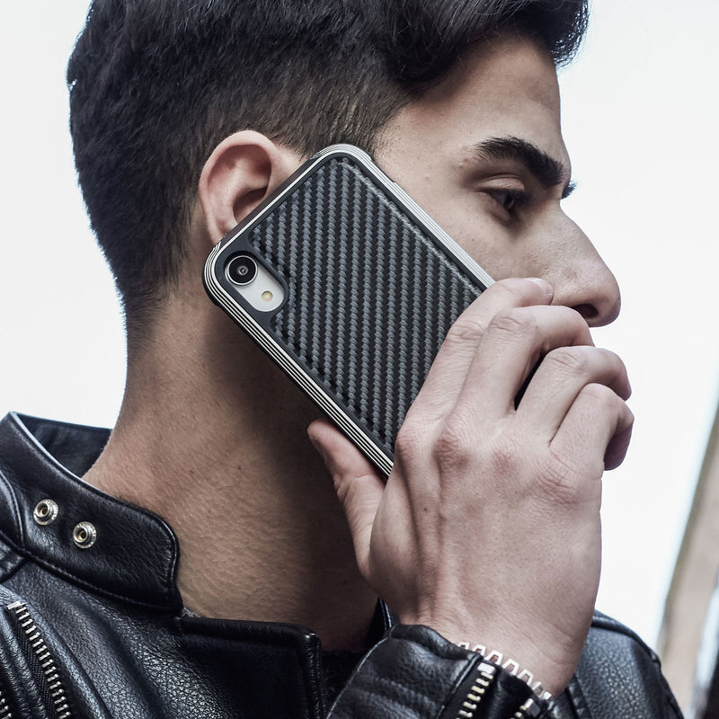 A person in a black leather jacket holds an iPhone XR with a Raptic LUX impact-resistant polycarbonate case to their ear.