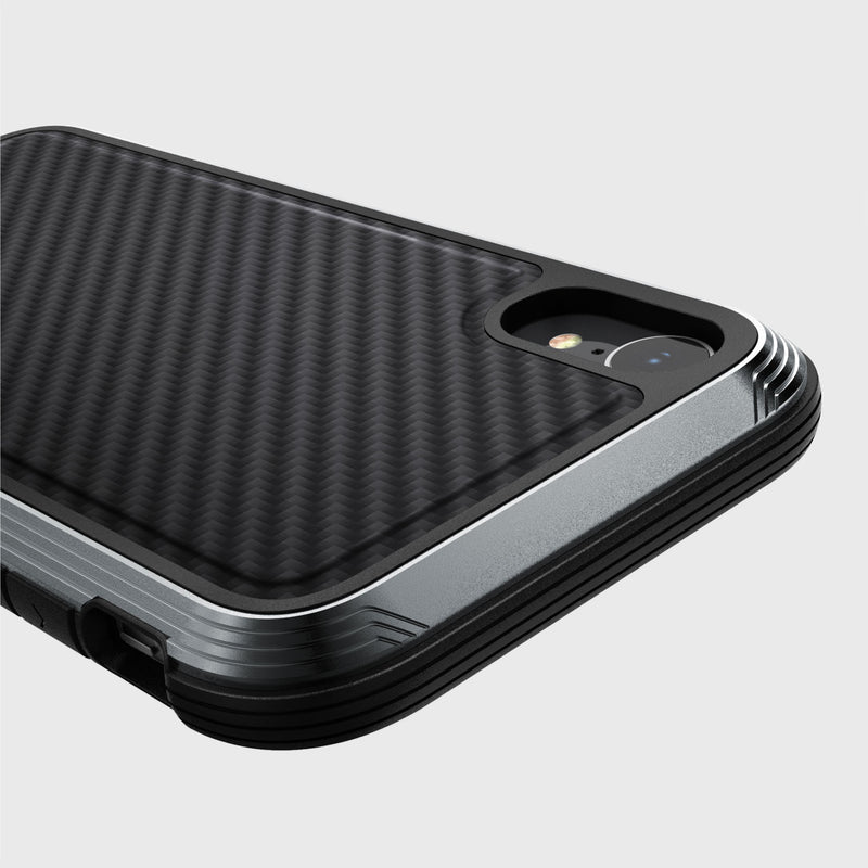 A close-up of the Raptic LUX iPhone XR case showcases its black carbon fiber textured surface, highlighting the rear camera area. The durable impact-resistant polycarbonate shell stands out against a plain backdrop.