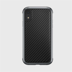The smartphone, set against a plain gray backdrop, is encased in the striking Raptic LUX iPhone XR case with a black carbon fiber pattern. It has an impact-resistant polycarbonate build and features a single rear camera and flash.