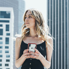 In an urban setting, a woman in a black top holds her smartphone with the Raptic SHIELD case for iPhone XR. The case, offering military-grade drop protection and shock absorption, blends style and security.