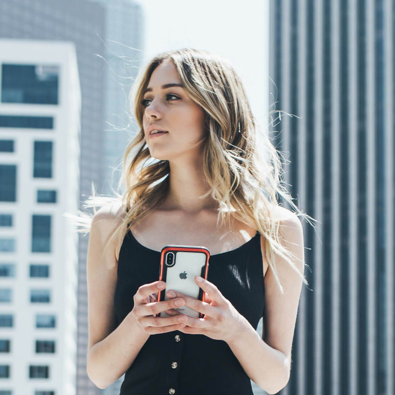 In an urban setting, a woman in a black top holds her smartphone with the Raptic SHIELD case for iPhone XR. The case, offering military-grade drop protection and shock absorption, blends style and security.
