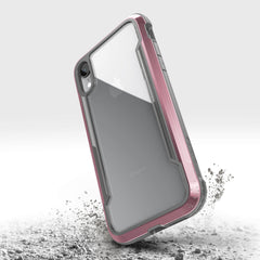 The iPhone XR, protected by a Raptic SHIELD case with pink edges, seems to bounce on a concrete surface, highlighting its military-grade drop protection.