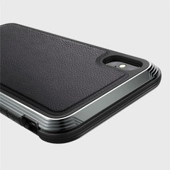Close-up of an iPhone XS Max in the Raptic LUX case, showcasing a textured black leather-like back and durable machined aluminum edges, highlighting the impact-resistant polycarbonate around the rear camera.