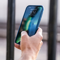 A person holding a blue iPhone 13 Pro Case - TERRAIN by Raptic on a railing, showcasing an eco-friendly gadget.