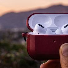 Hand holding open case of airpods pro with blurred cityscape in the background at dusk.