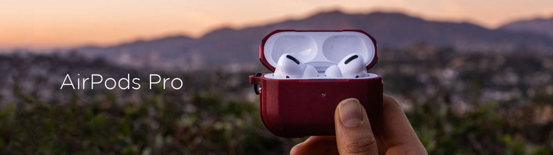 Hand holding open case of airpods pro with blurred cityscape in the background at dusk.