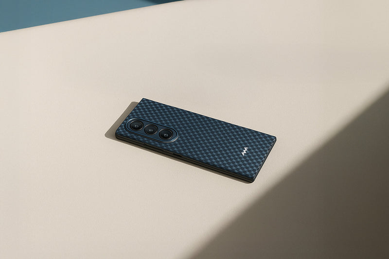A black smartphone with a textured, carbon-fiber-like case and three rear cameras lies on a beige surface under soft lighting.