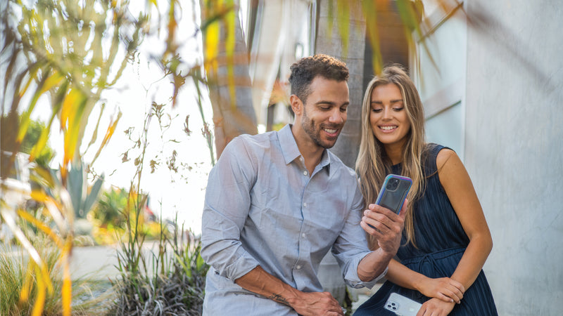 A man holding an iphone 12 in a raptic case with a woman overlooking his shoulder