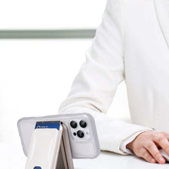 A person in a white suit sits at a table. In the foreground, a smartphone displays a visible bank card in its Raptic Air Wallet, an iPhone Magnetic Wallet by Raptic.