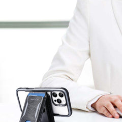 A person in a white suit sits at a desk with a smartphone in a black Raptic Air Wallet case and a MagSafe Stand positioned in the foreground.