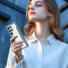 A person in a white blouse holds a Samsung Galaxy S25 in a Raptic SHIELD case, featuring military-grade drop protection, while looking upwards.