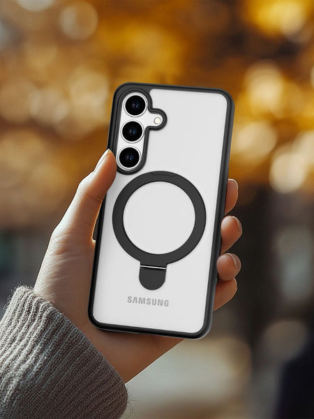 A hand holds a Samsung Galaxy S25 in a white Raptic Air Stand case with a black circular grip, providing military-grade drop protection. Blurred autumn foliage appears in the background.