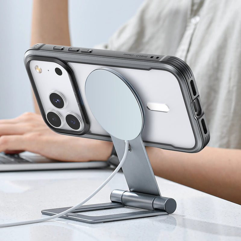 A person types as their iPhone 17, in the Raptic Shield Case by Raptic, charges securely on a horizontal metal MagSafe stand.