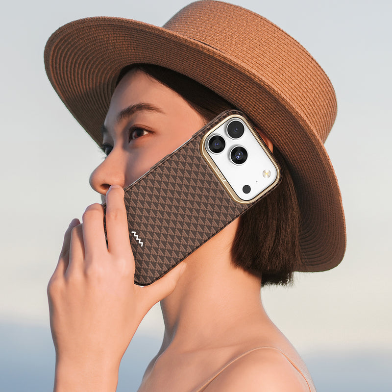 A person in a wide-brimmed hat holds the Raptic iPhone 17 Aramid Fibre Case - Skin-Origin, a MagSafe-compatible, ultra-light military-grade cover, to their ear as if making a call against a light sky background.