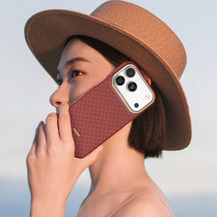 A woman in a wide-brimmed hat holds an iPhone with a Raptic Skin-Origin Aramid Fibre Case to her ear, as if making a call.