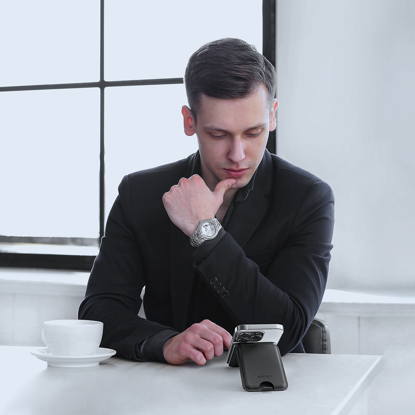 A man in a suit sitting at a table with a Raptic iPhone Wallet MagSafe KickStand.