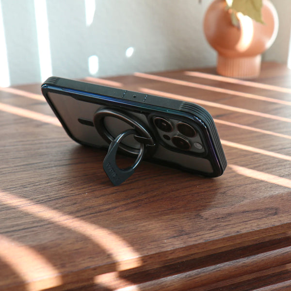 A Raptic MagSafe Ring Stand - Gunmetal-compatible phone is sitting on a table with a Raptic MagSafe Ring Stand - Gunmetal.