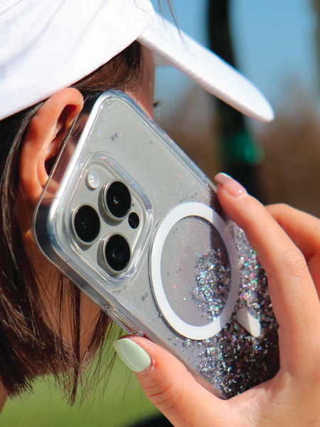 A woman wearing a golf hat while holding an iPhone 15 Starburst Glitter MagSafe Case - Bryten by Raptic that supports wireless charging.