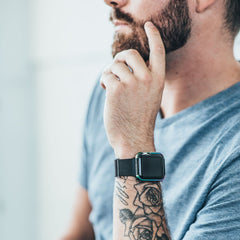A man in a gray t-shirt with a tattooed forearm thoughtfully rests his hand on his chin, showcasing the Raptic Apple Watch 40mm Case - EDGE for added style and scratch protection.
