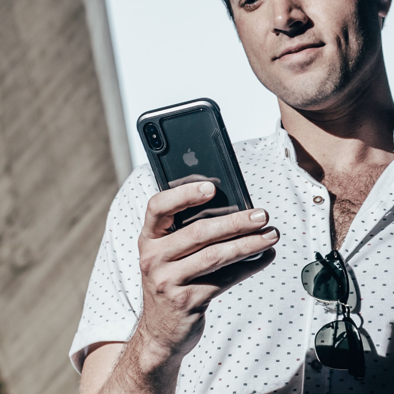 A man holding an iPhone X/XS while looking at it, protected by the Raptic SHIELD case.