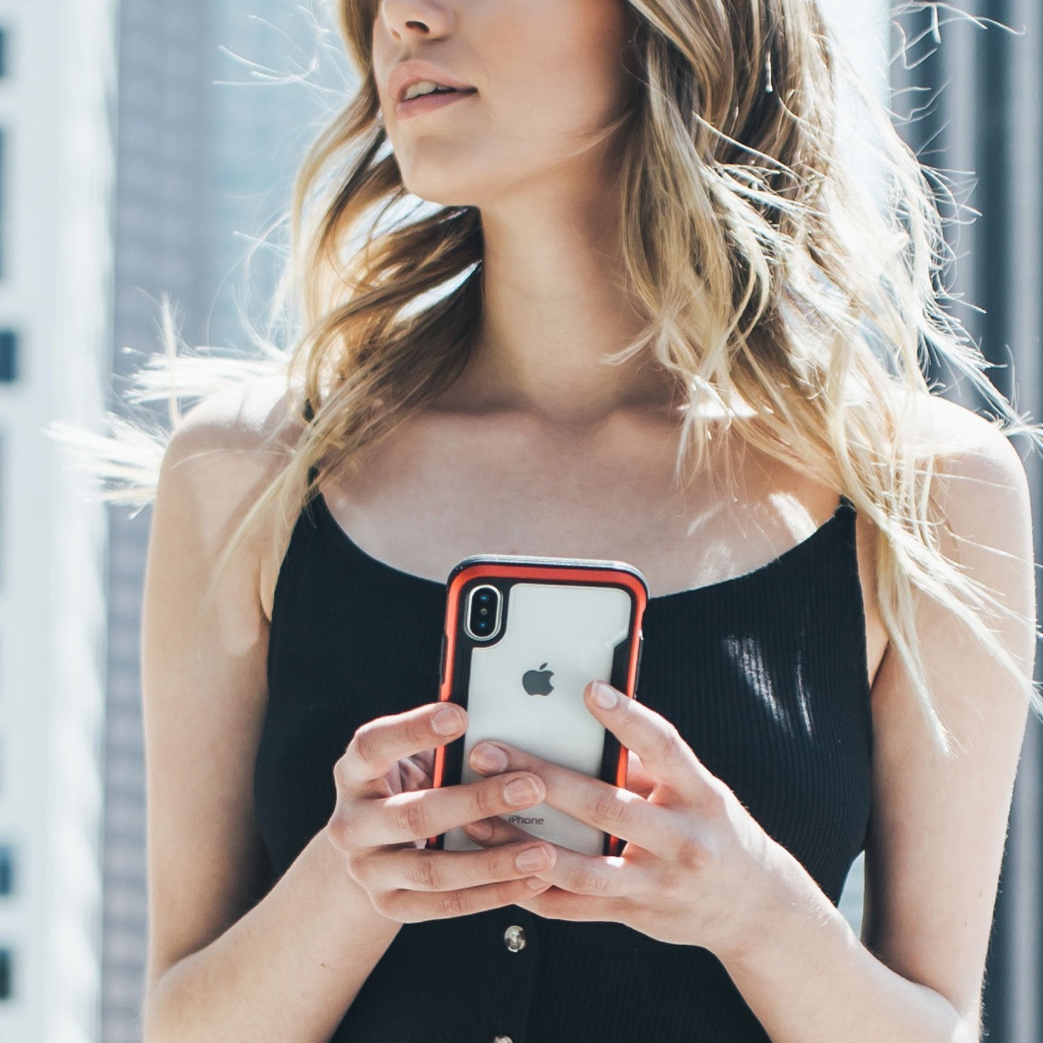 A woman holding an iPhone XS Max in front of a building while showcasing the drop protection provided by the Raptic Shield case.