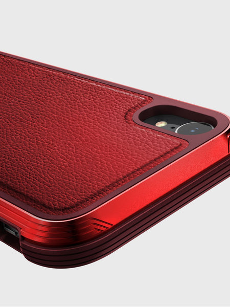 Close-up of the Raptic iPhone XR Case - LUX, showcasing its red textured finish with camera cutout and stylized edges on a gray background. The impact-resistant polycarbonate design combines durability and style.