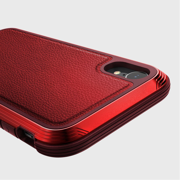 Close-up of the Raptic iPhone XR Case - LUX, showcasing its red textured finish with camera cutout and stylized edges on a gray background. The impact-resistant polycarbonate design combines durability and style.