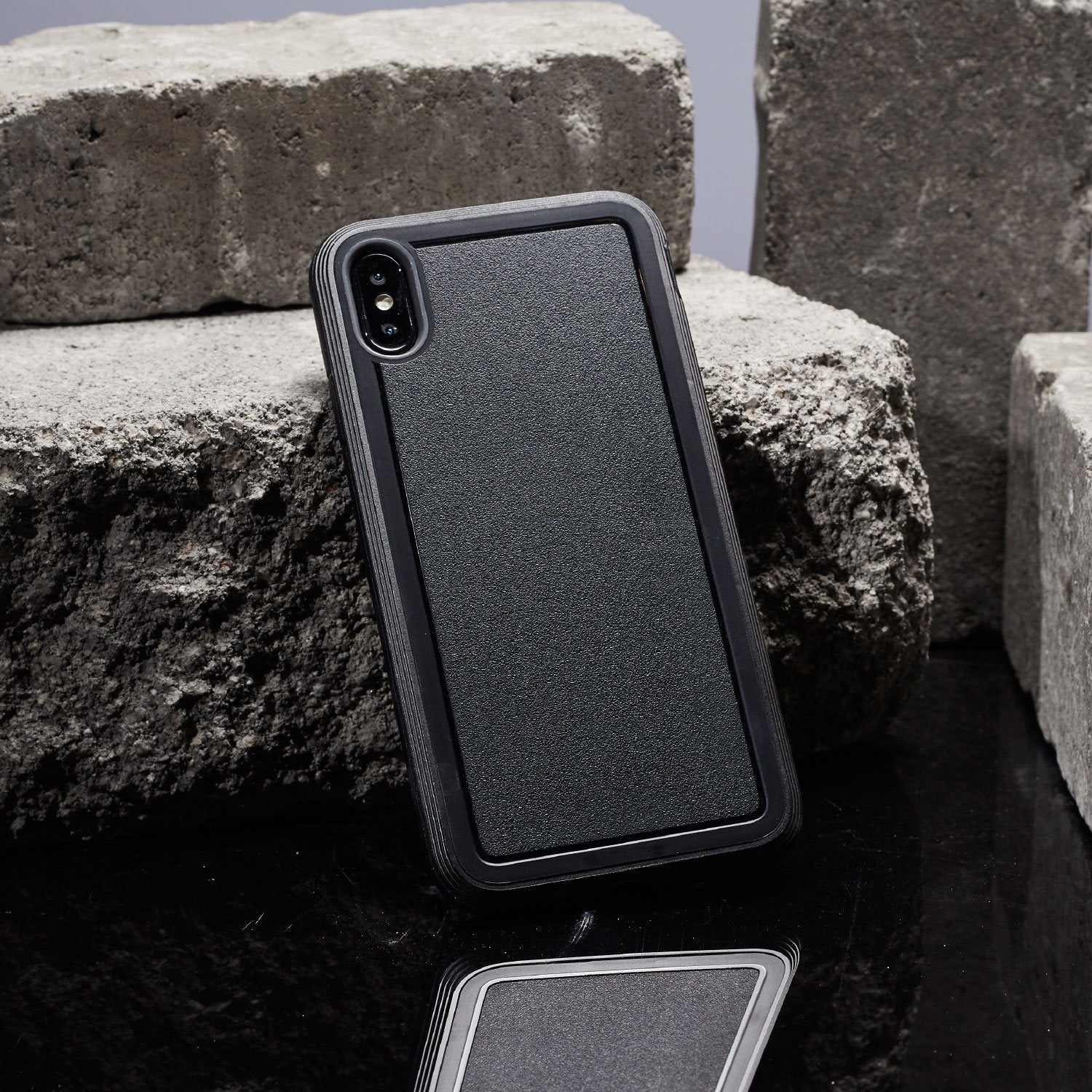An X-Doria black iPhone Xs Defense Ultra Black case, designed to meet the MIL-STD-810G Standard for device protection, sits on top of some rocks.