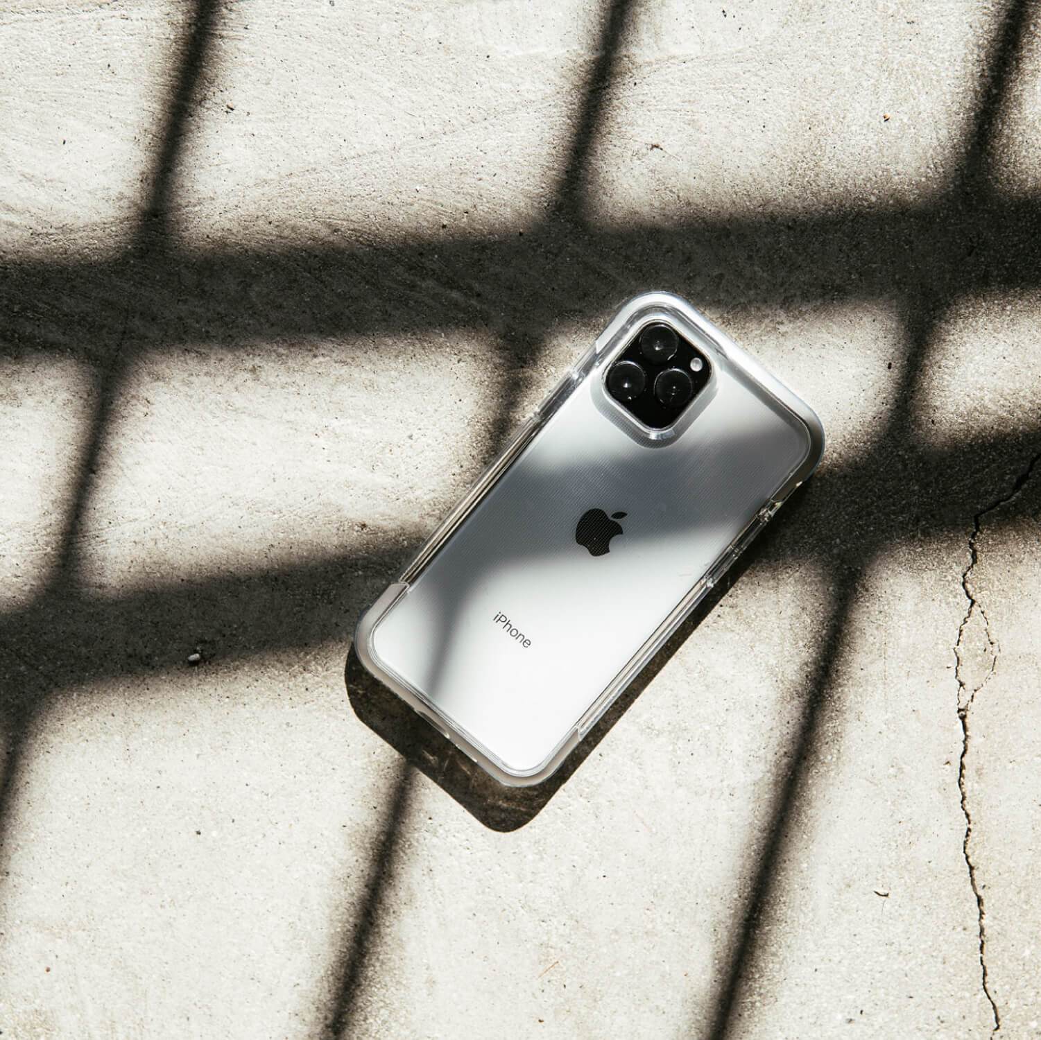 A white iPhone 11 Pro Max with Raptic AIR case is resting on a concrete floor, offering 13 foot drop protection.