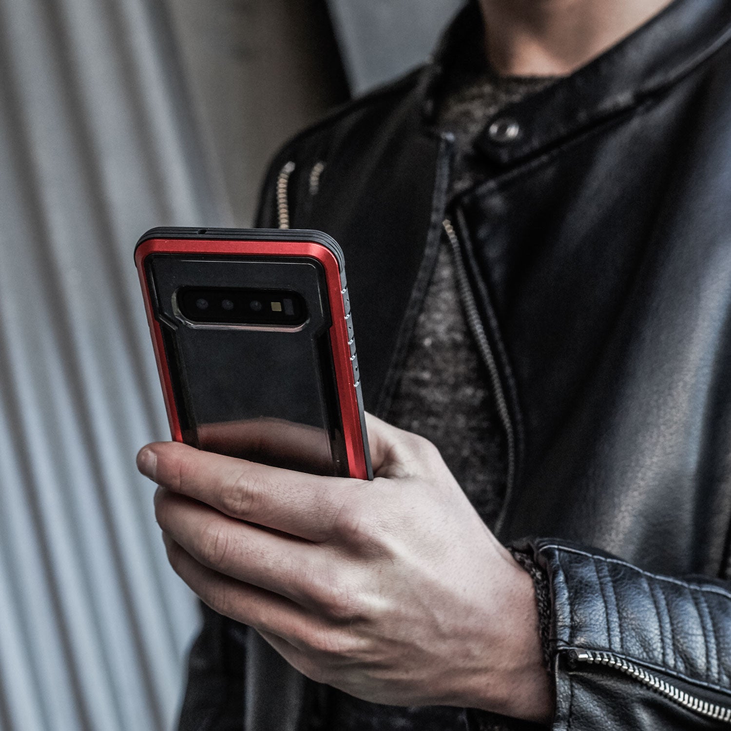 A man in a leather jacket is holding an X-Doria Samsung Galaxy S10 Plus Case Raptic Shield Red.