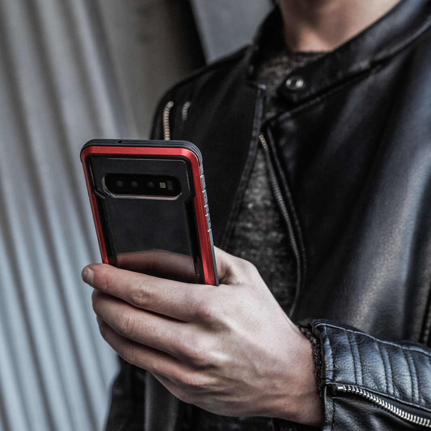 A man in a leather jacket is holding an X-Doria Samsung Galaxy S10e Case Raptic Shield Red with drop protection.