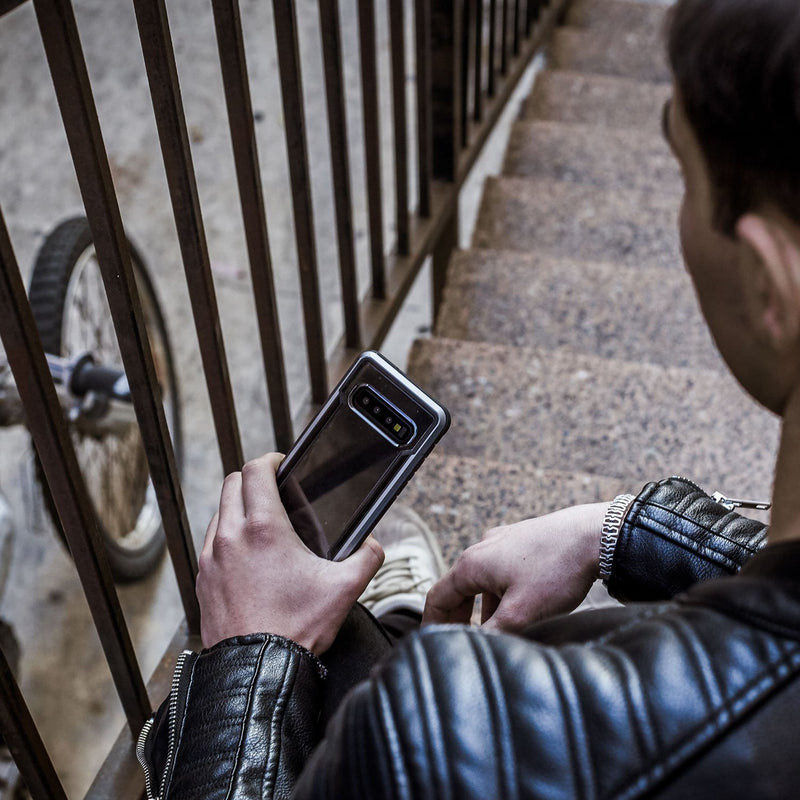A man in a leather jacket confidently holding a Raptic Shield Black case for the Samsung Galaxy S10e phone.