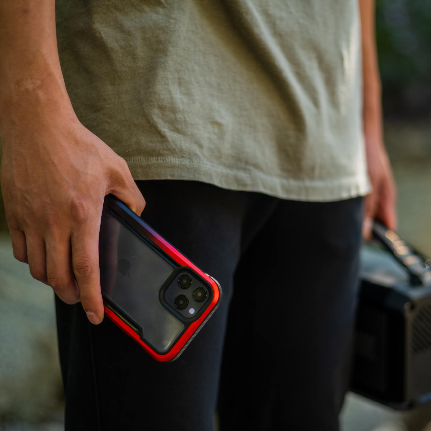 A person holding an iPhone 12 Pro Max with a Raptic SHIELD case for 13' foot drop protection attached to it.