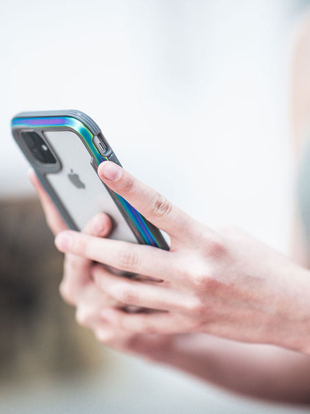 Someone holding an iPhone 11 with Raptic's SHIELD case enjoys peace of mind while focusing on the screen. The vibrant cover complements the phone's aluminum alloy design and remains compatible with wireless charging for seamless connectivity.