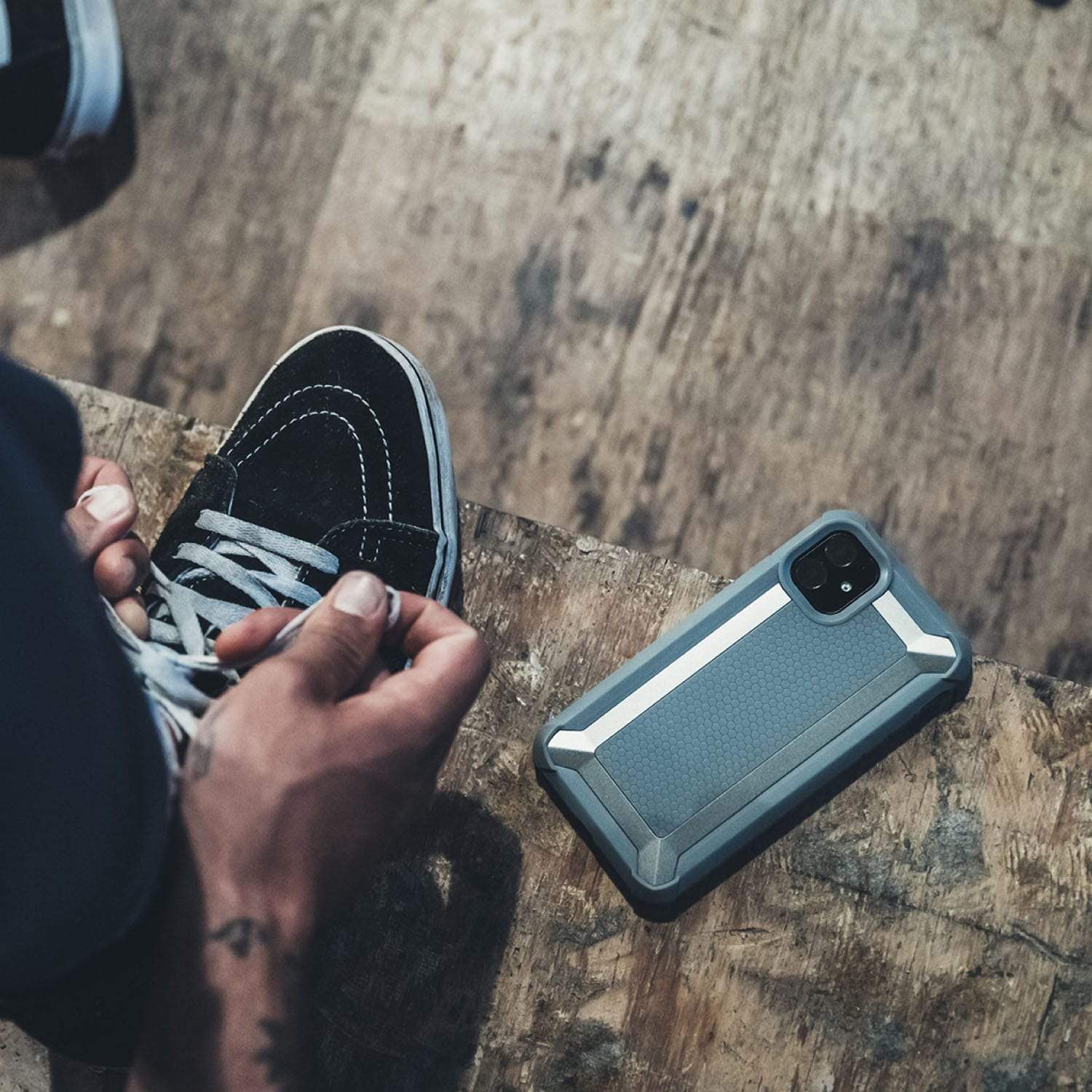 A person holding an iPhone 11 Pro Case - TACTICAL by Raptic next to a pair of sneakers.
