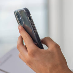 A person holding an iPhone 12 Pro Max Case - AIR by Raptic in their hand with 4-metre drop protection and wireless charging compatibility.
