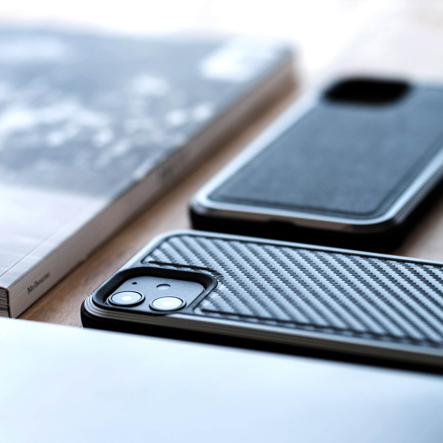 The Raptic Lux iPhone 12 Mini Case - LUX, known for its luxury design and reliable 3-metre drop protection, is placed on a table alongside a book.