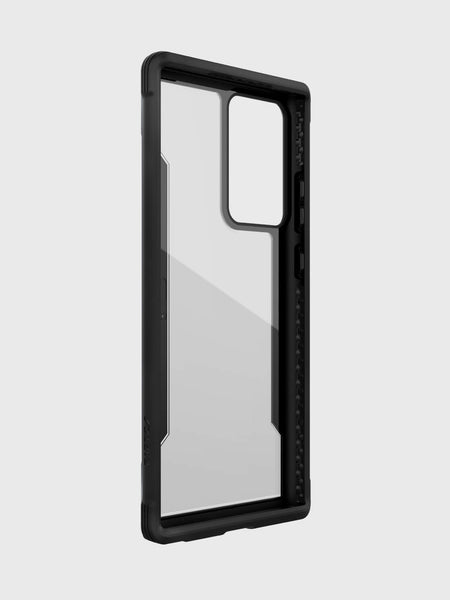 The Raptic Shield case for Galaxy Note 20 Ultra in Black features a clear back with a black bumper frame, designed for phones with a rectangular camera cutout. Displayed on a plain gray background, this case from Raptic provides military-grade drop protection while staying compatible with wireless charging.