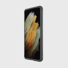 A Samsung Galaxy S21 Ultra with an X-Doria Raptic Shield Iridescent case and abstract wallpaper is angled against a plain light gray background, showcasing its military-grade drop protection.