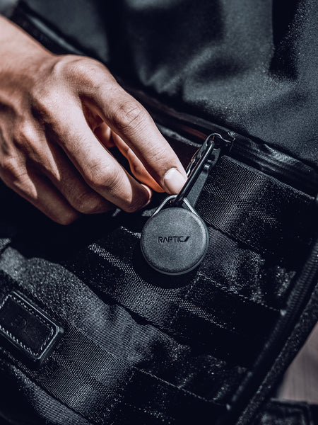 Apple AirTags encased in a Raptic Link case with carbines hanging off a stylish black bag