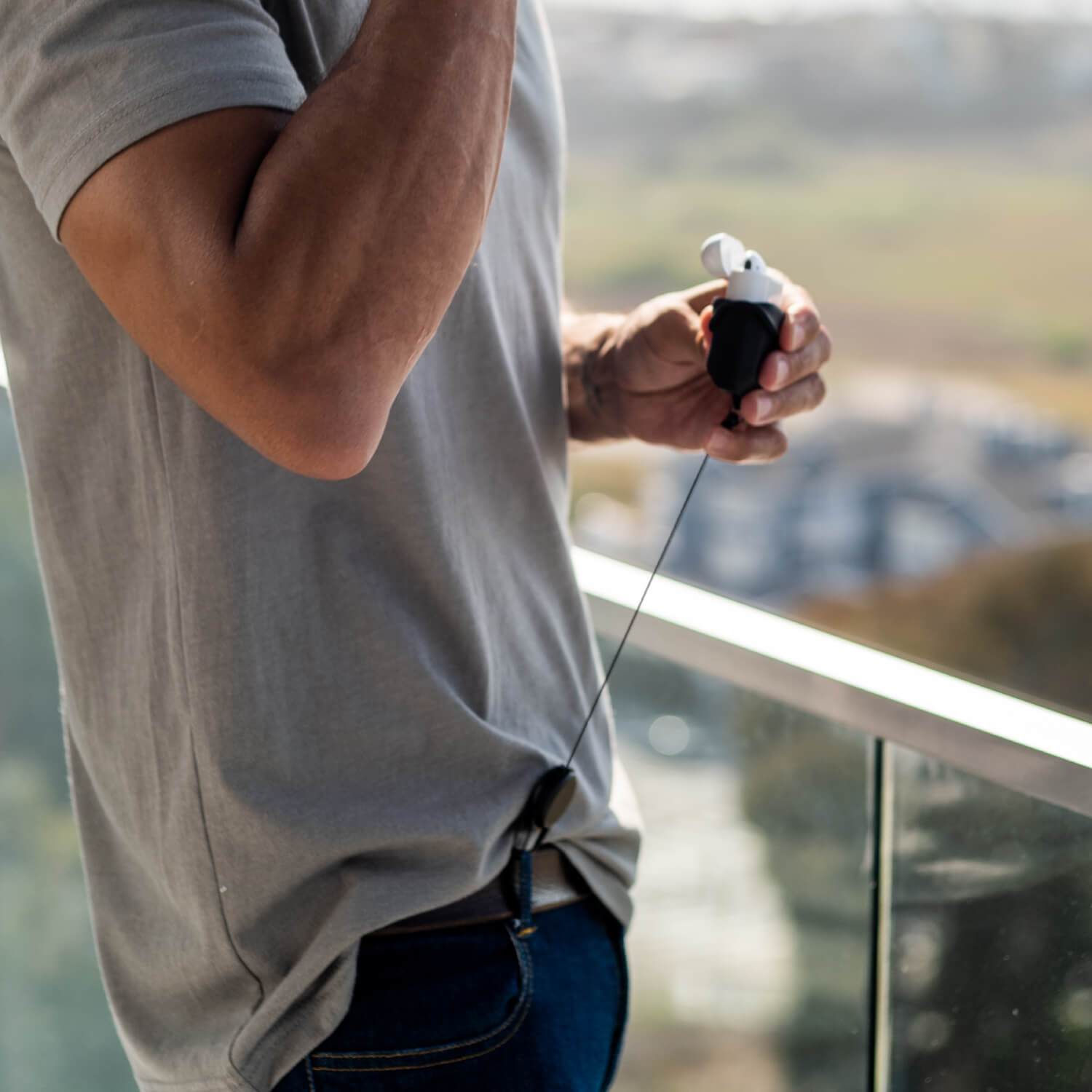 A man using a Raptic carabiner to secure his Apple AirPods Pro Case - RADIUS while standing on a balcony.