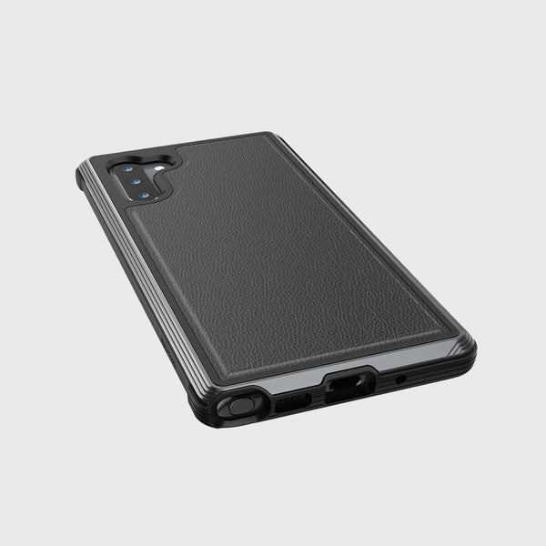 A Samsung Galaxy Note 10+ in a Raptic Lux Black Leather case is on a light gray surface, highlighting its rear cameras and charging port. This military-grade case offers drop protection and wireless charging compatibility, making it durable and convenient for daily use.